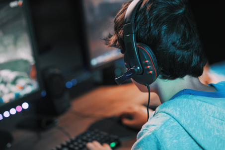 Young gamer wearing a headset and playing online multiplayer video games on his computer.